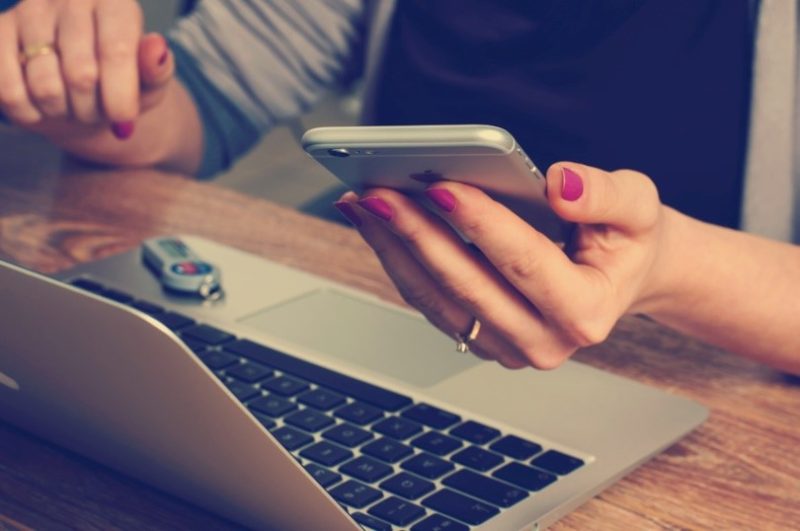 woman holding a phone in front of her laptop