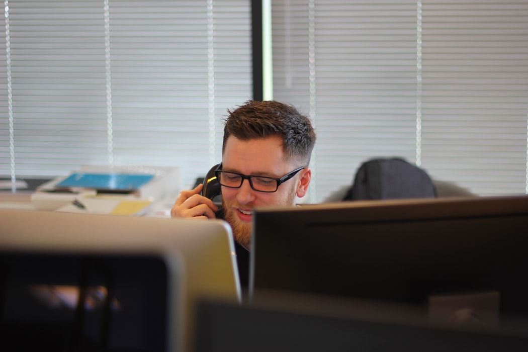 man talking on the phone behind a computer and cluttered desk